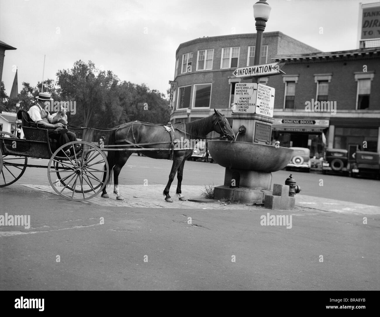1920s cavallo beve dal trogolo di acqua nel centro di CLAREMONT NEW HAMPSHIRE CON INFORMAZIONI E SEGNO DI DIREZIONE POST Foto Stock