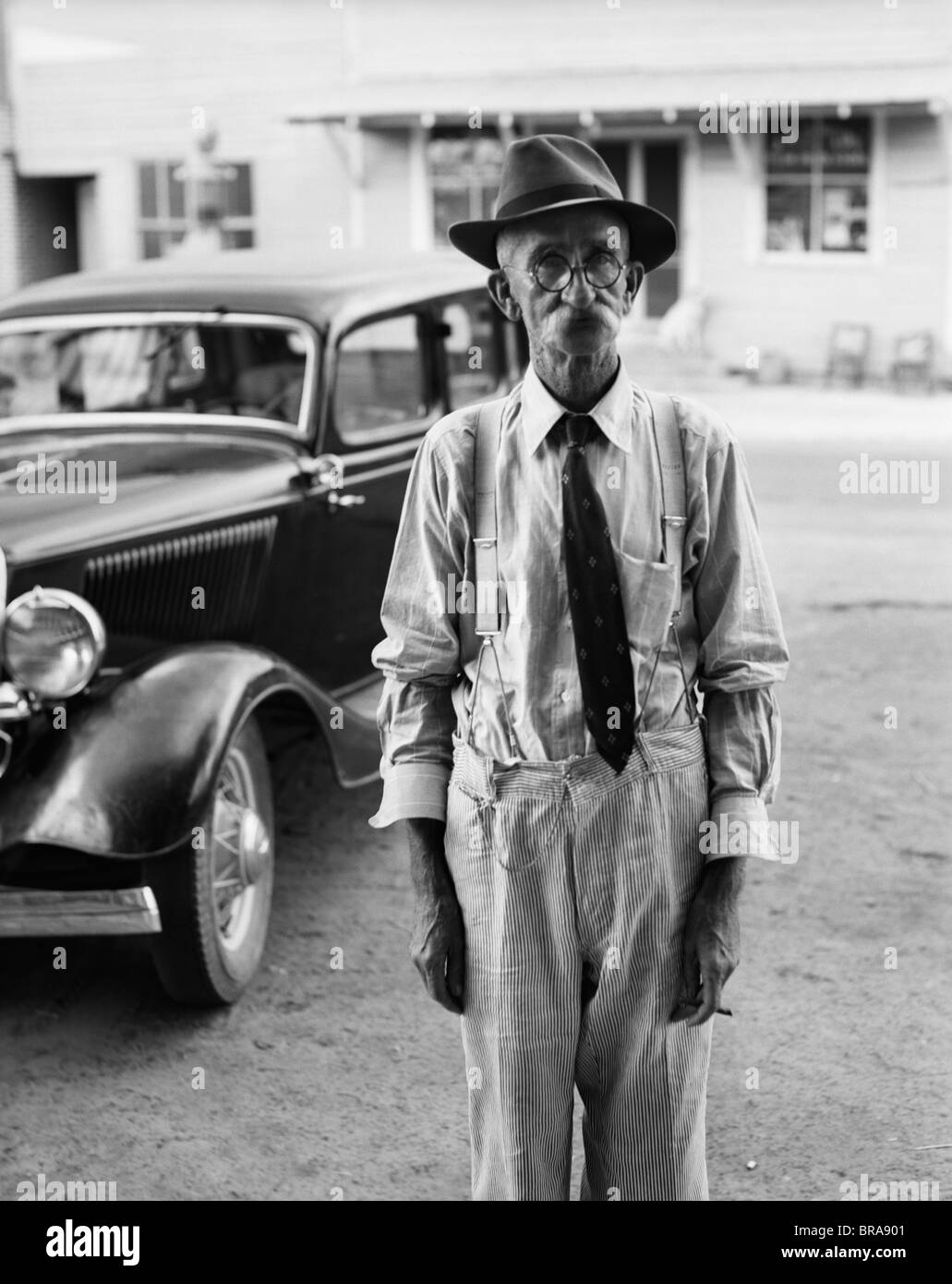 1930s Ritratto di vecchio uomo che indossa gli occhiali HAT TIE & calze autoreggenti AUTO IN BACKGROUND Foto Stock