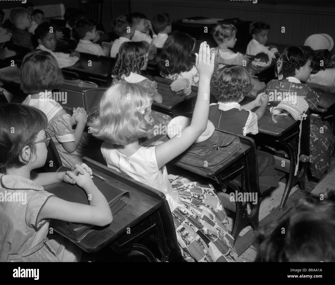 Anni Cinquanta GLI STUDENTI DELLA SCUOLA ELEMENTARE IN AULA ragazza bionda alzando la mano Foto Stock