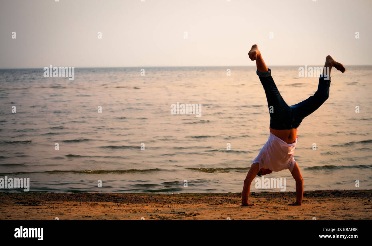L'uomo facendo handstand sulla spiaggia al tramonto Foto Stock
