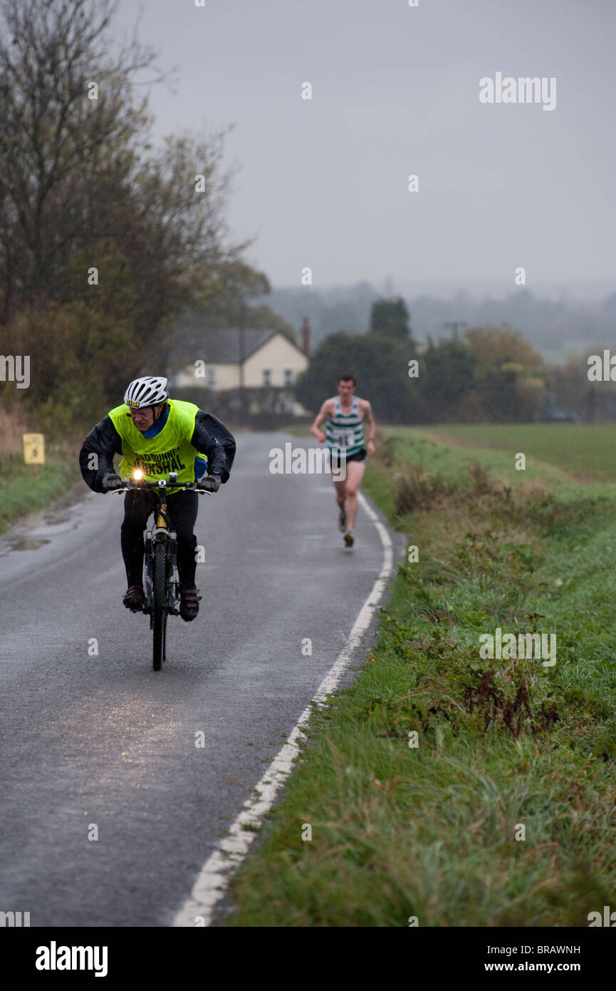 Un ufficiale di gara su una bicicletta di battaglie il vento e la pioggia  come egli accompagna il filo lone runner della Billericay 10km di corsa su  strada Foto stock - Alamy