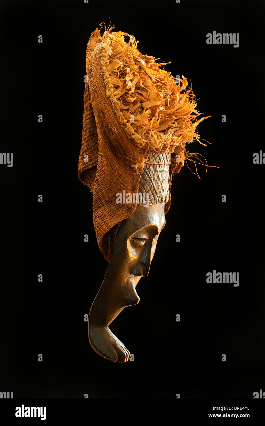 Legno scolpito tribale Africano, maschera di legno scuro con paglia e tela copricapo. Africa, tribù , foto dal lato in studio Foto Stock