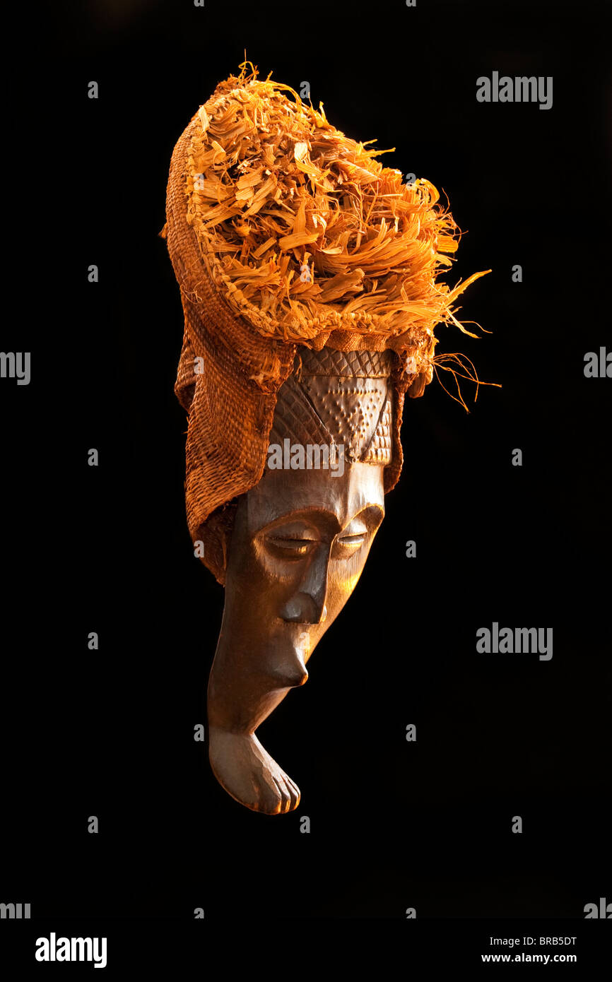 Legno scolpito tribale Africano, maschera di legno scuro con paglia e tela copricapo. Africa, tribù , foto dal lato in studio Foto Stock