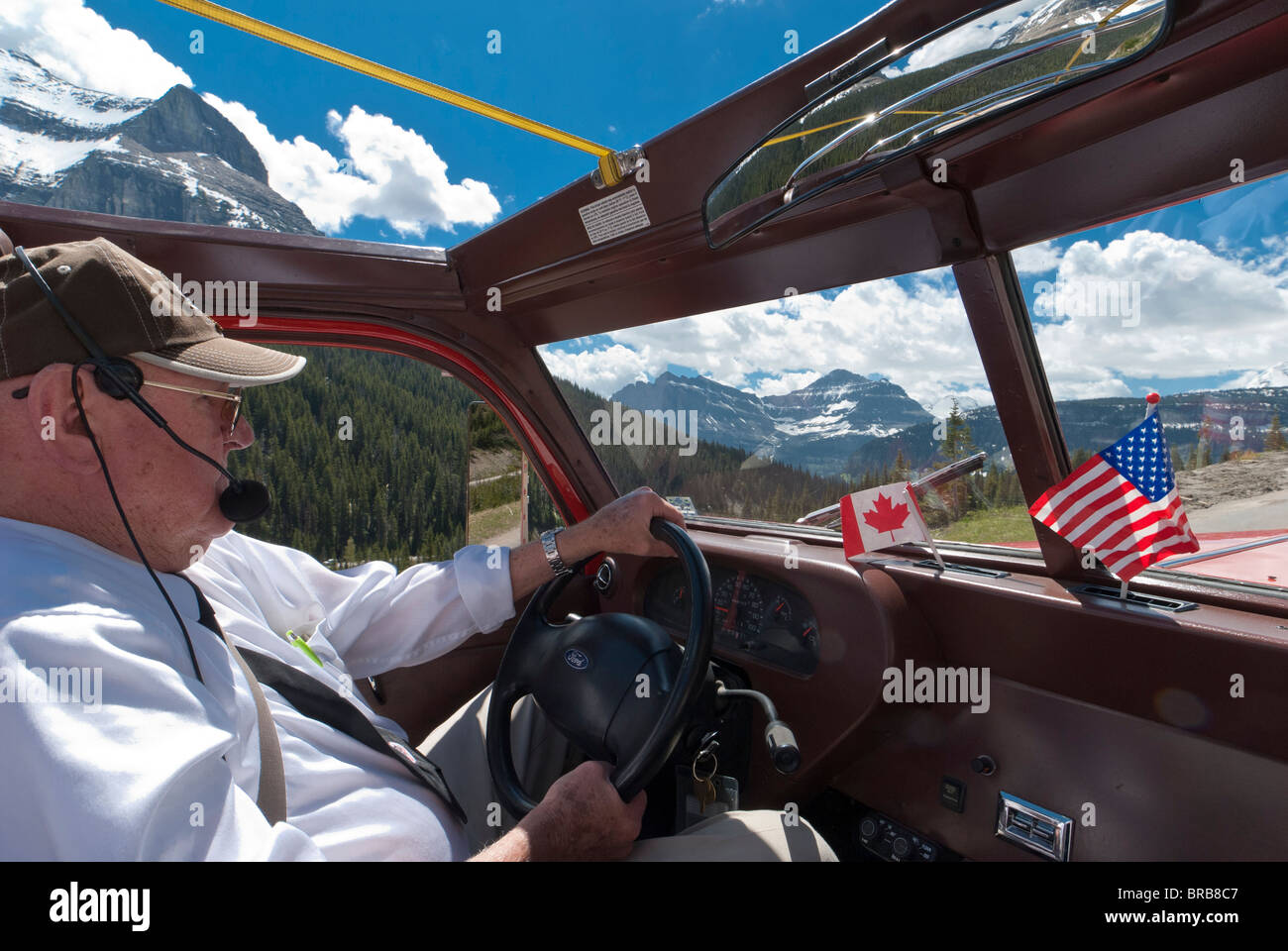 Howard Carpenter al volante di un bus rosso, andando-per-il-Sun Road, il Parco Nazionale di Glacier, Montana. Foto Stock