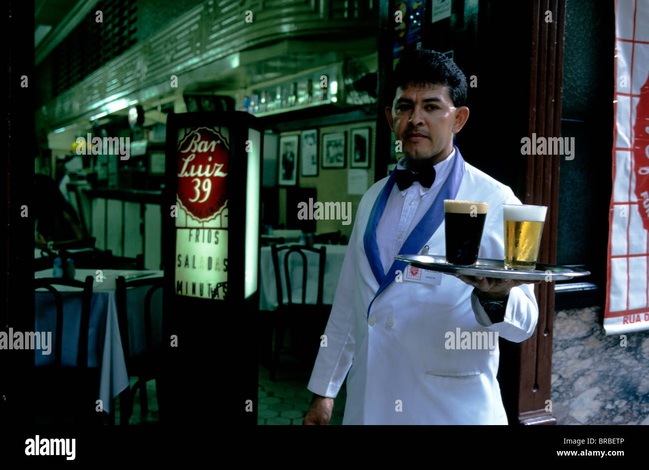 Un cameriere in piedi al di fuori di Rio de Janeiro del famoso Bar Luiz con un vassoio di birra - lager e stout. Foto Stock