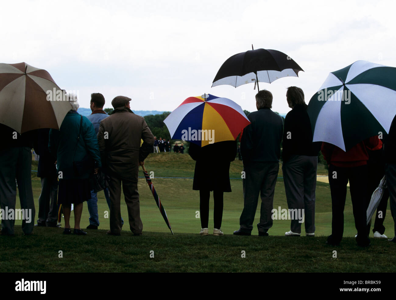 Gruppo di persone a guardare una partita di golf con ombrelloni sollevato Foto Stock