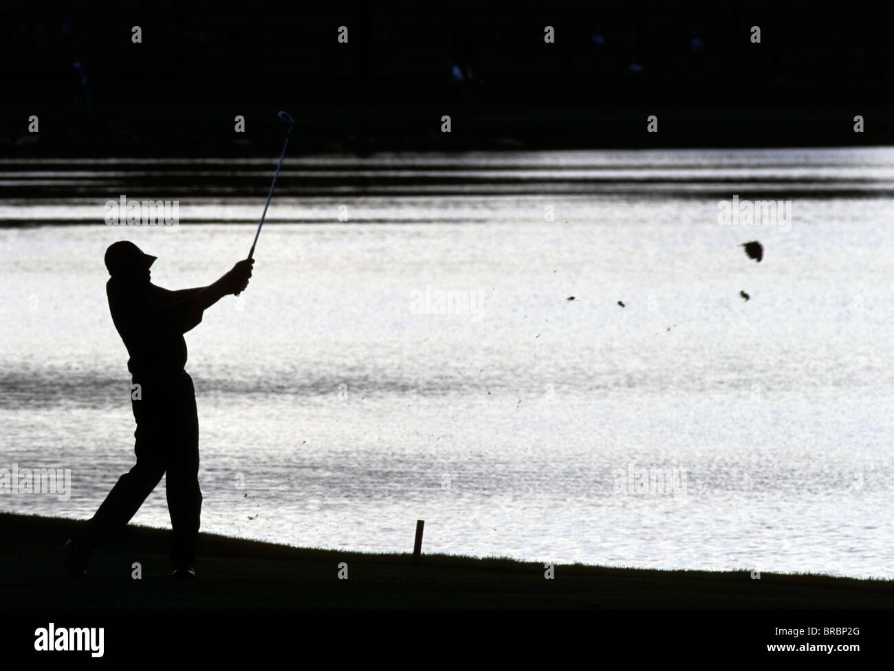 Silhouette di un golfista oscillando la sua club sullo sfondo di acqua riflettente Foto Stock