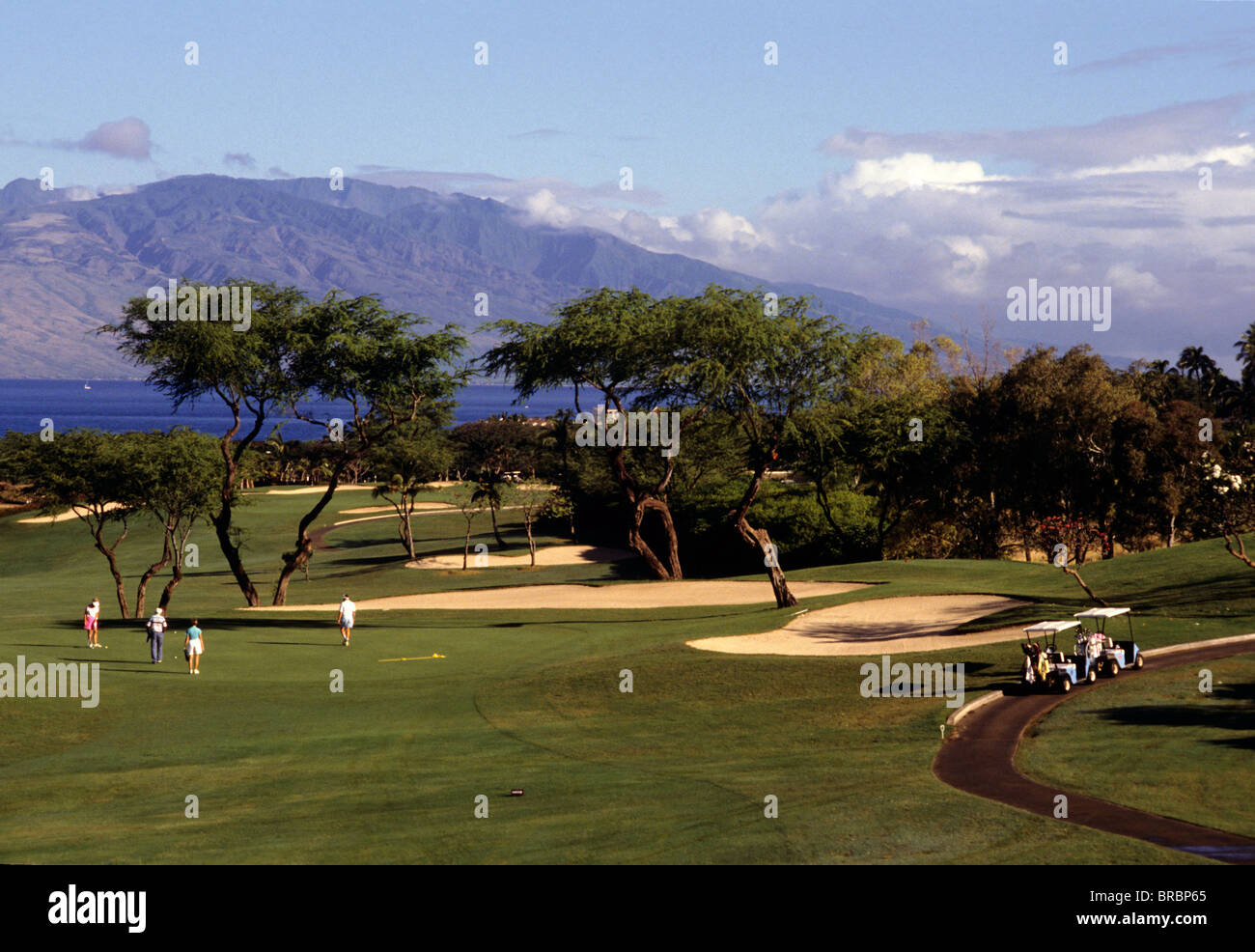 Prospettiva a lungo termine di un foresome giocando a golf sul green con le montagne e il mare in background Foto Stock