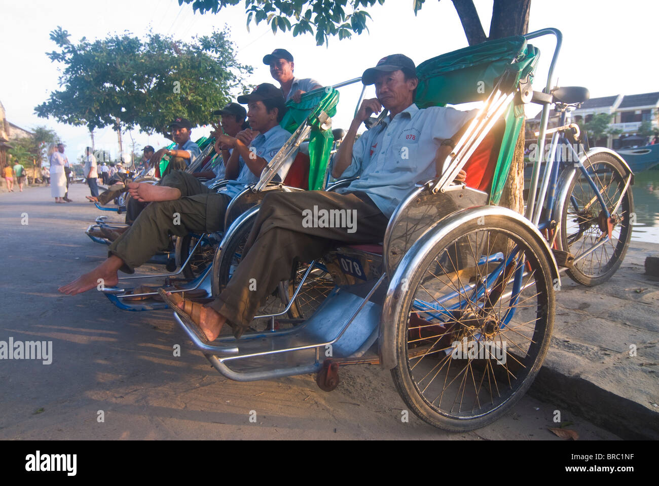 In rickshaw driver in seduta il riscio di attesa per i clienti, Hoi An, Vietnam, Indocina Foto Stock