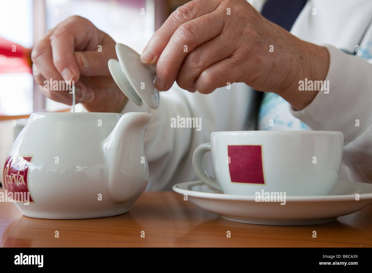 Persona in un caffè Mania café agitazione tè in una teiera con una tazza e piattino. Regno Unito, Gran Bretagna. Foto Stock