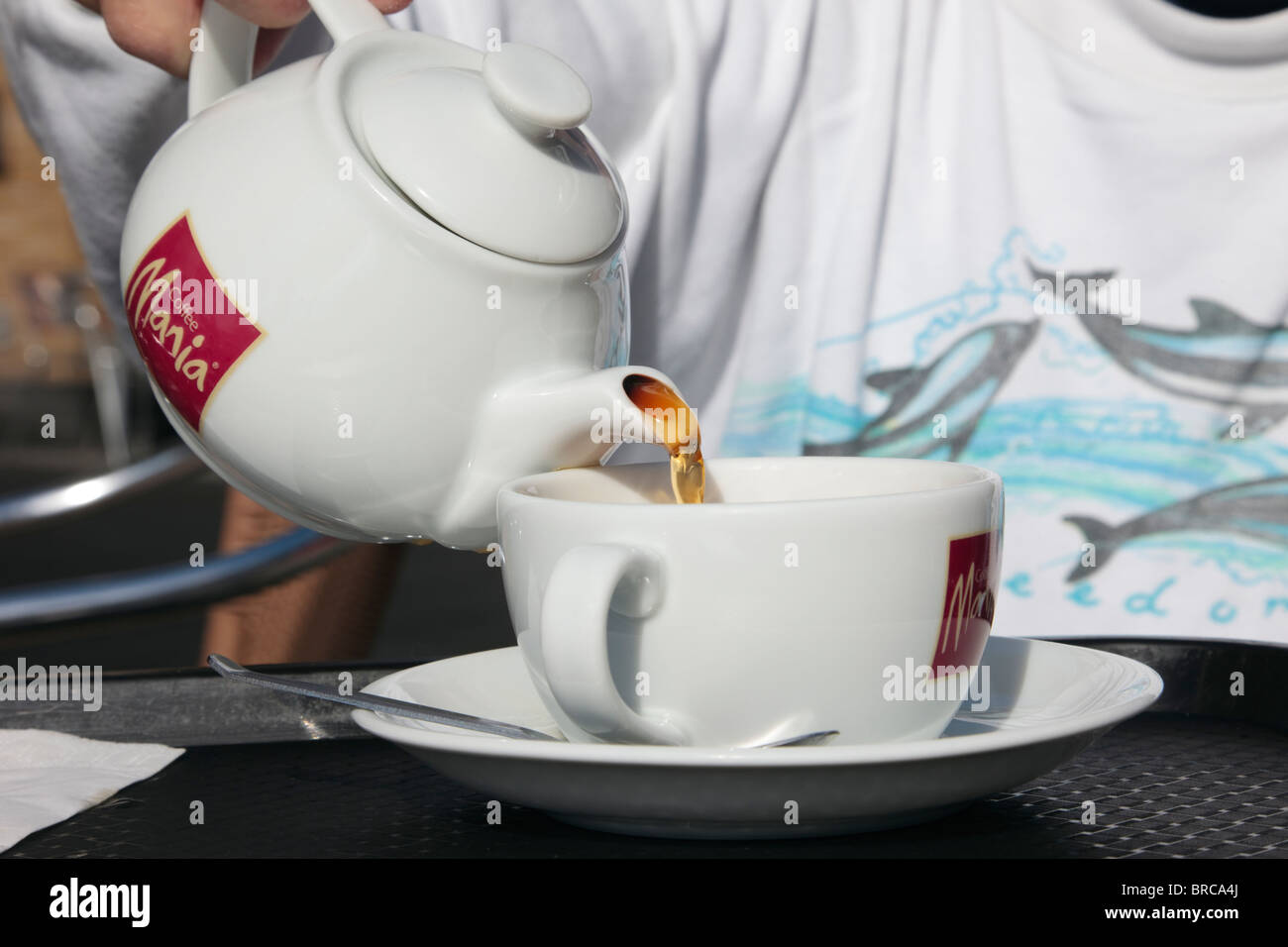 Persona in un caffè Mania café versando il tè da una teiera in una tazza e piattino. Il Regno Unito, l'Europa. Foto Stock