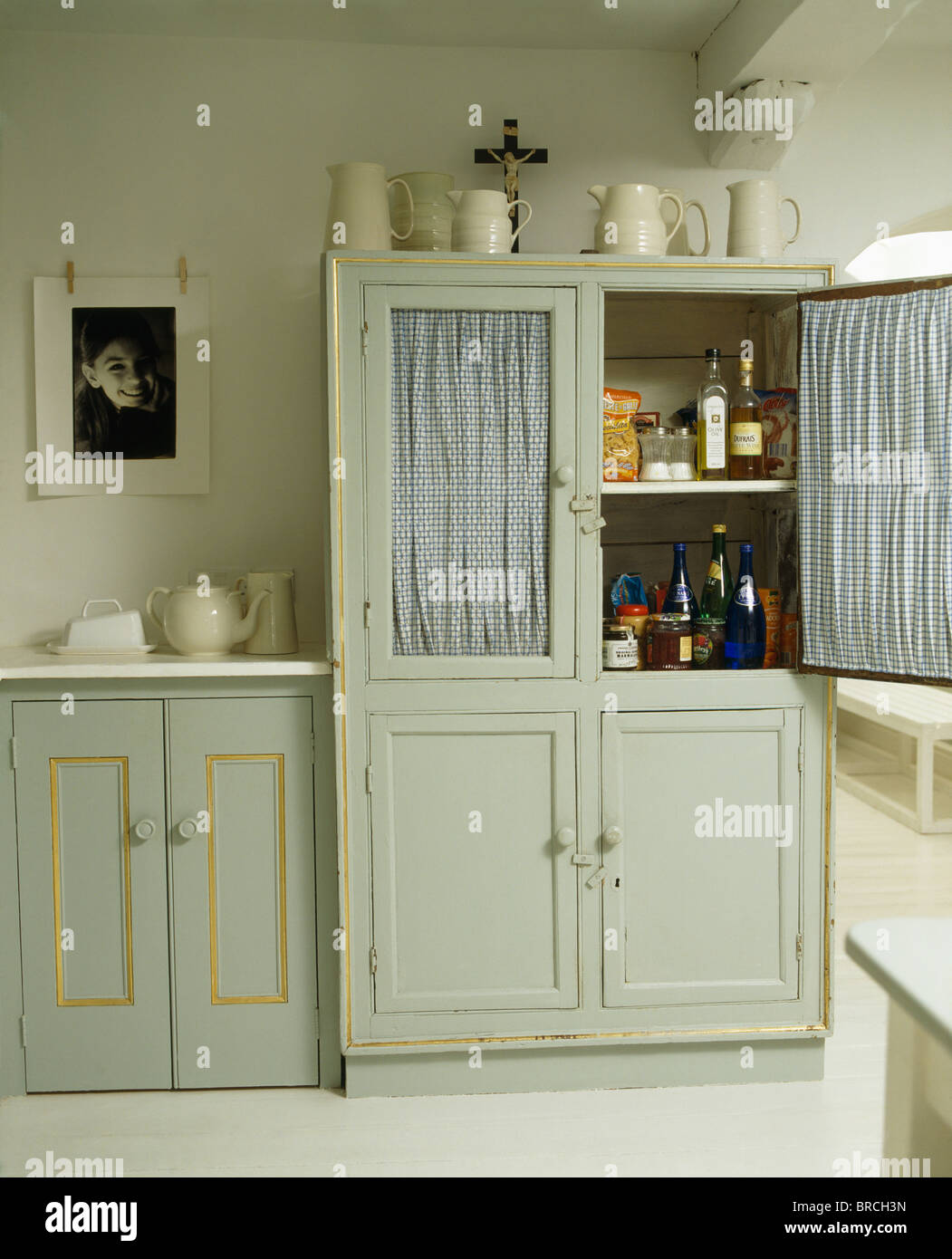Dotato di colore grigio pallido comò con tende dietro le porte vetrate in cottage cucina Foto Stock