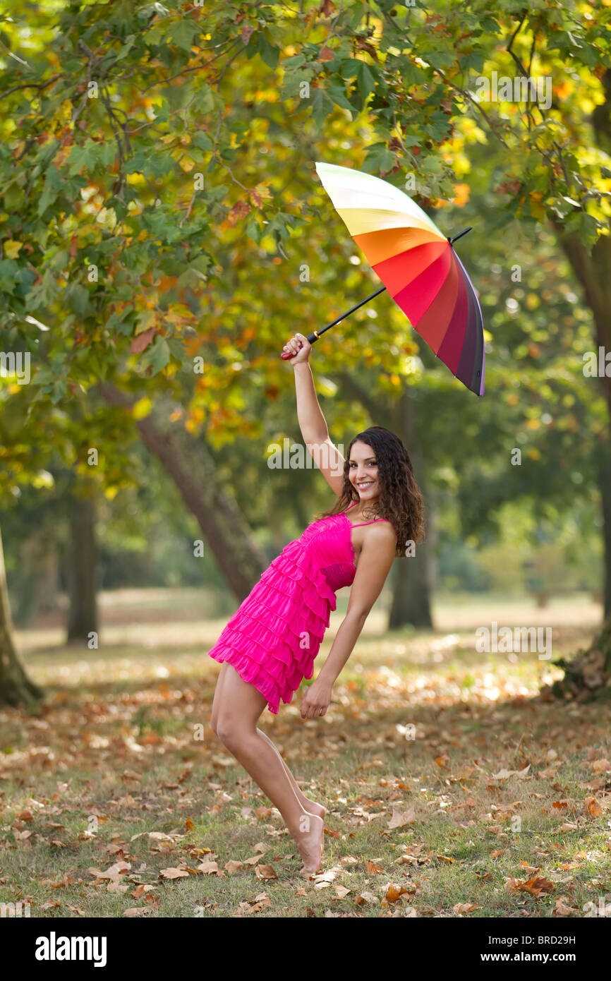 La ragazza a piedi nudi in piedi in punta di piedi indossando abiti rosa con ombrello arcobaleno in posizione di parcheggio Foto Stock