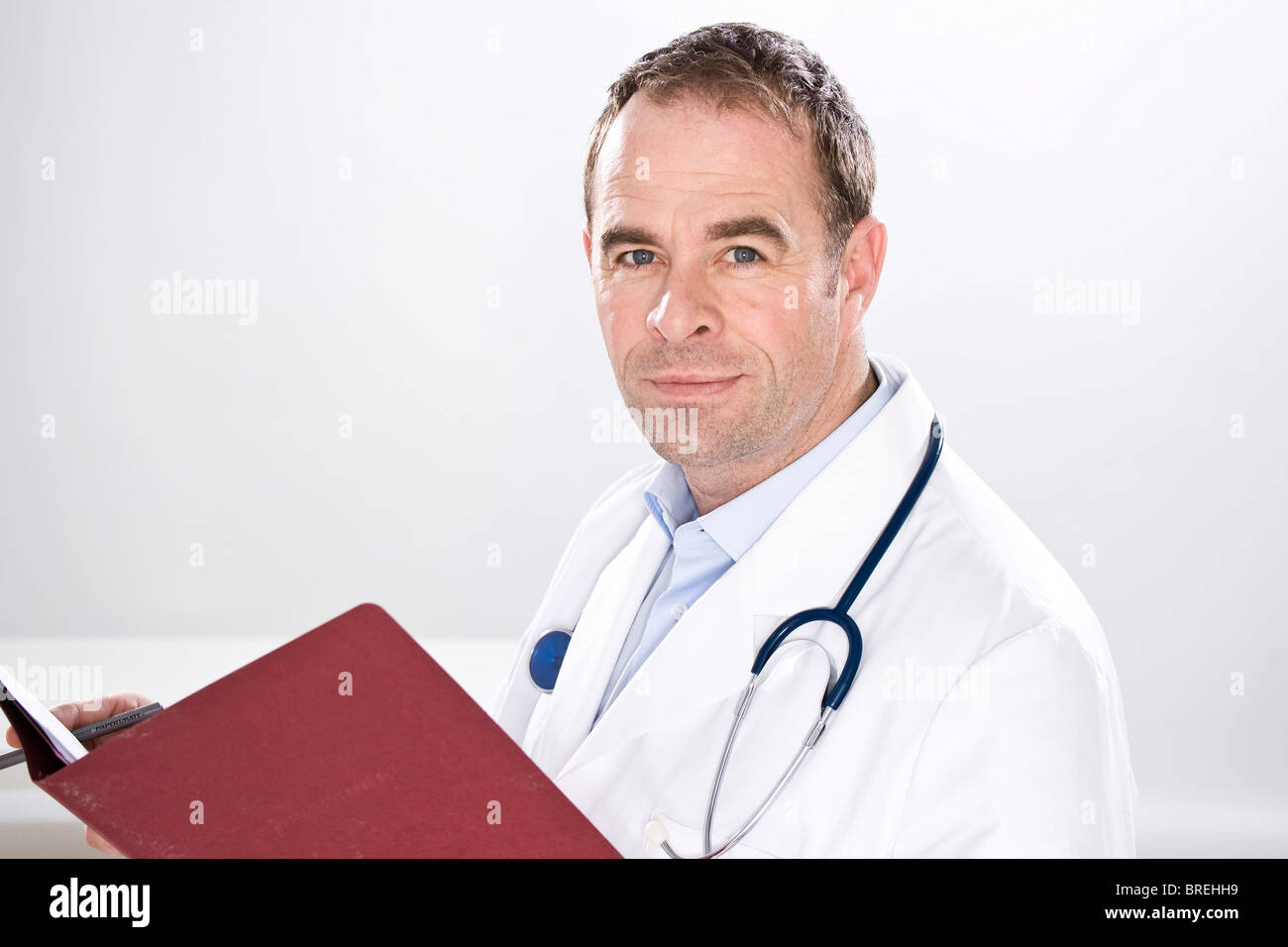 Uomo sorridente indossando medical scrubs, con uno stetoscopio, tenendo in mano un file Foto Stock