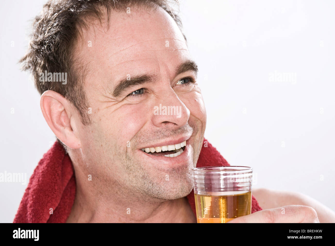 Uomo sorridente con un asciugamano attorno alle sue spalle, bere un bicchiere di succo di frutta Foto Stock