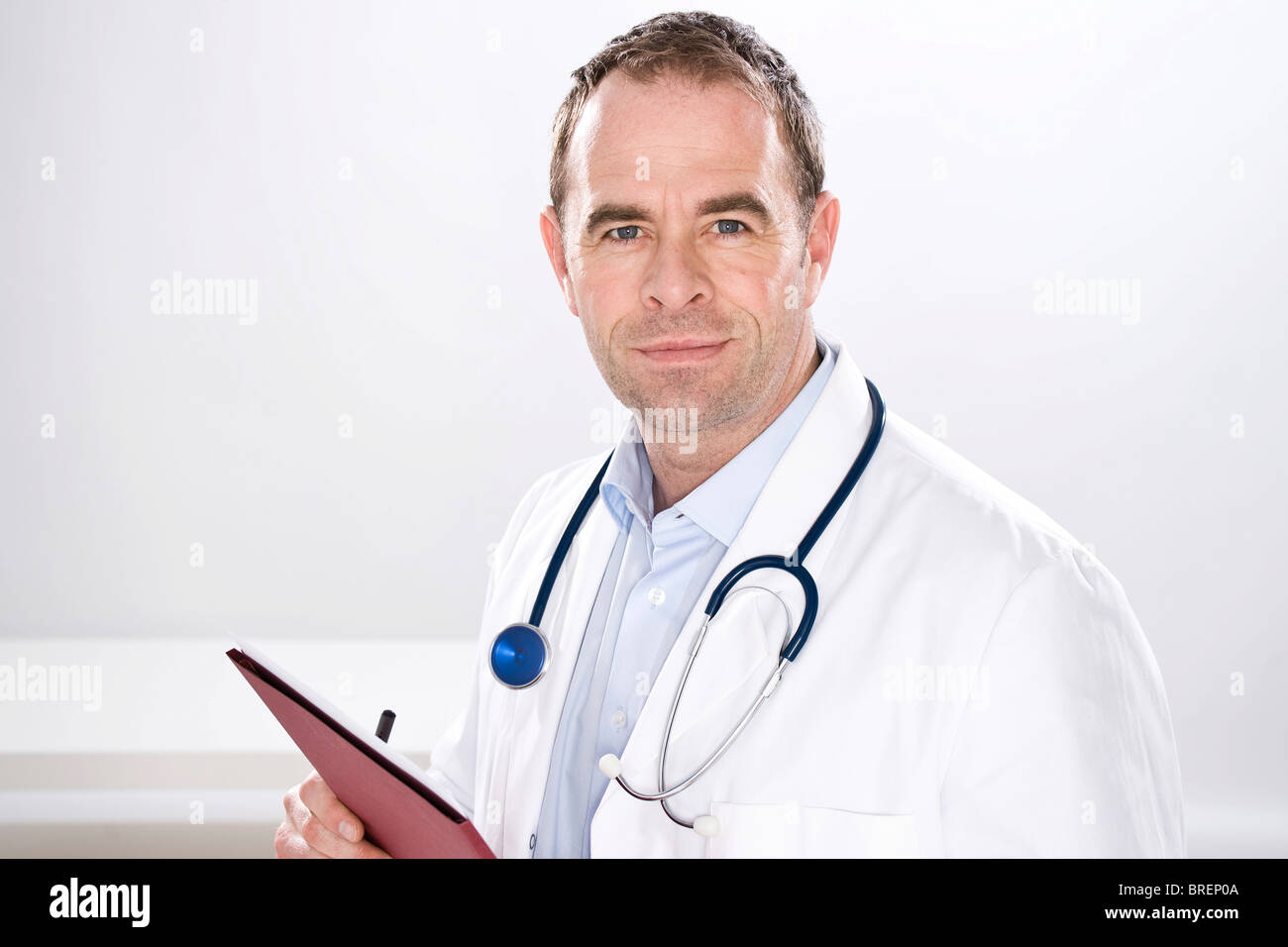 Uomo sorridente indossando medical scrubs, con uno stetoscopio, tenendo in mano un file Foto Stock