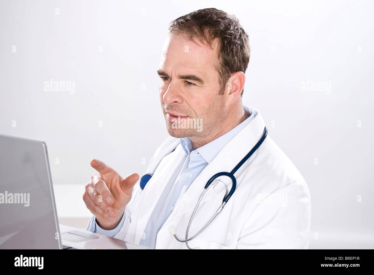 Uomo sorridente indossando medical scrubs, con uno stetoscopio, guardando il computer Foto Stock