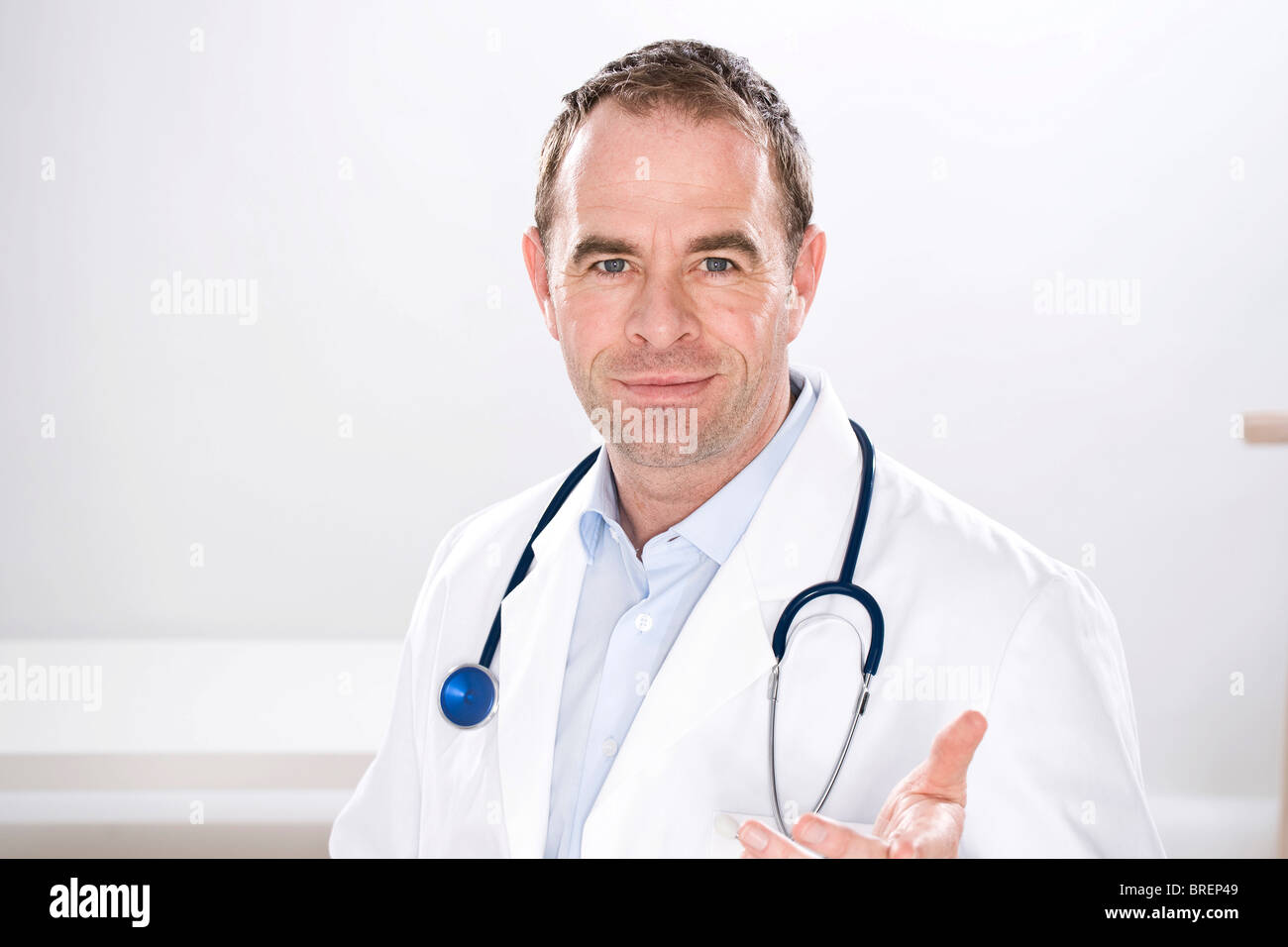 Uomo che indossa medical scrubs, tenuto in mano ed estrarlo dalla parte anteriore, guardando questioningly Foto Stock