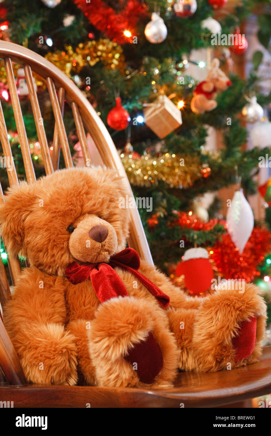 Natale interno con un orsacchiotto di peluche su una sedia davanti a un albero di natale Foto Stock