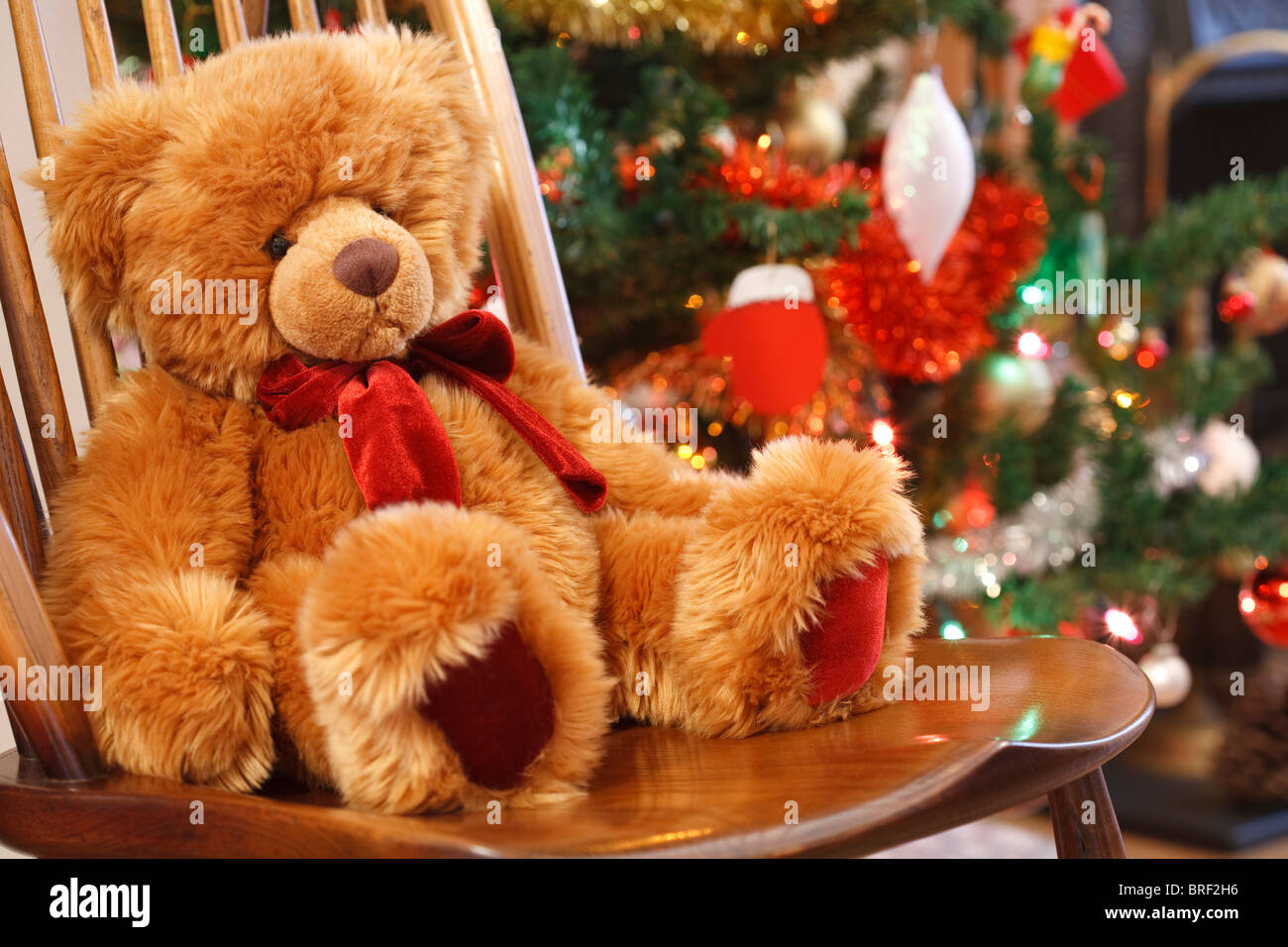 Mercatino di Natale in scena con un orsacchiotto di peluche su una sedia davanti a un albero di natale Foto Stock