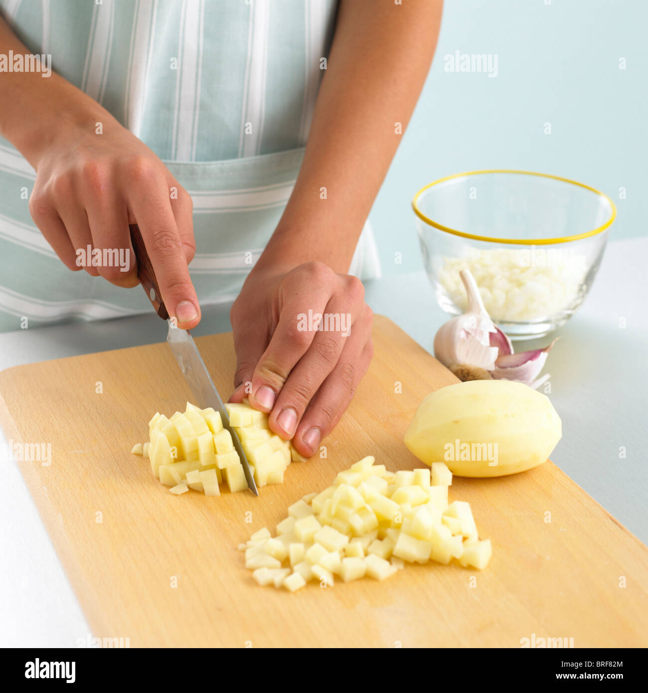 Donna fare cubetti di patate crudo sul tagliere Foto Stock