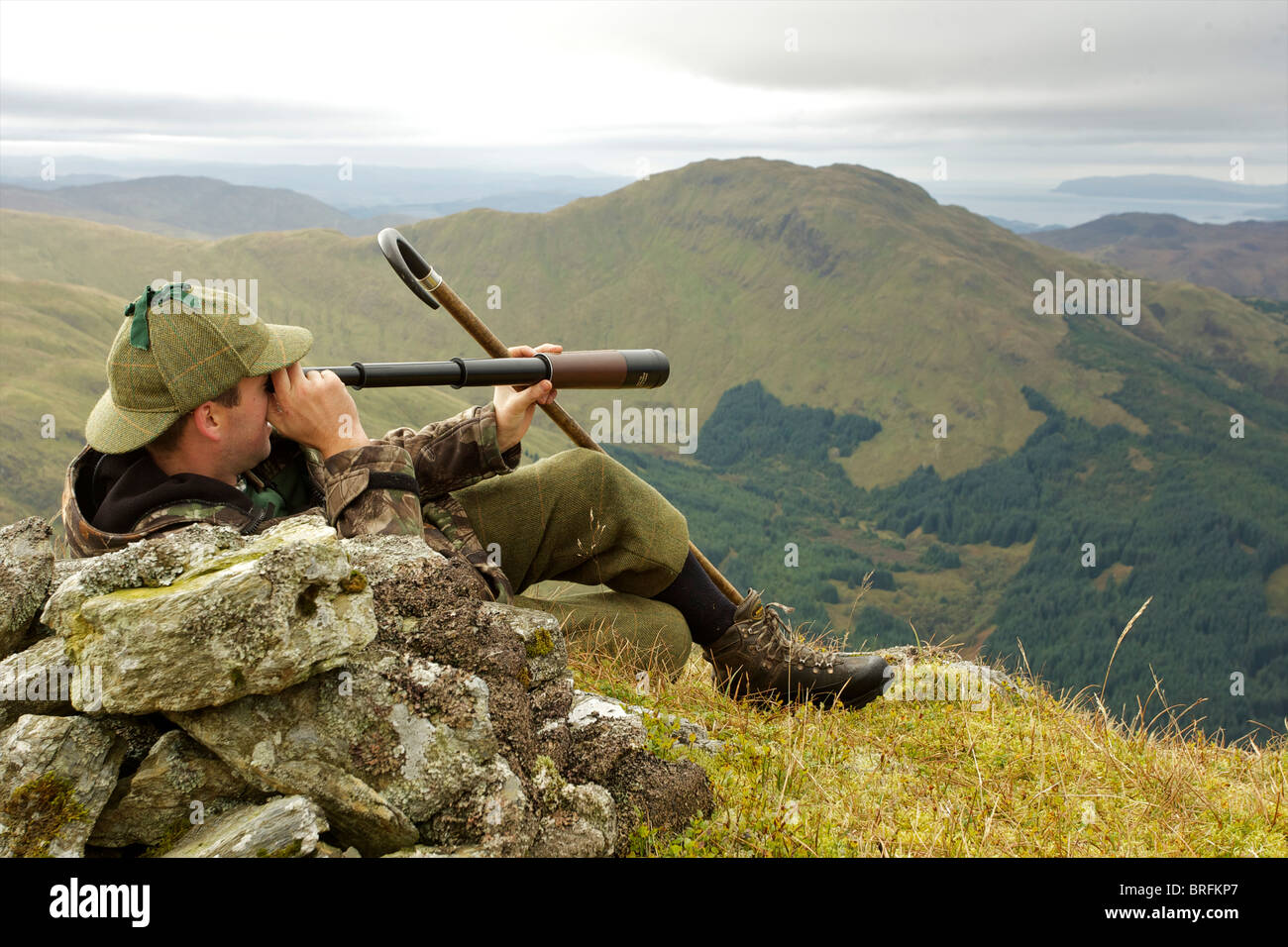 Cervi scozzese stalker sulla cima di una montagna di spionaggio per cervi utilizzando tre disegnare telescopio Foto Stock
