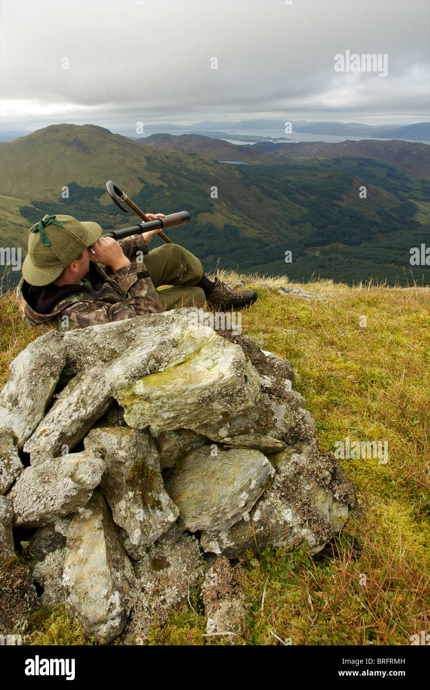 Cervi scozzese stalker sulla cima di una montagna di spionaggio per cervi utilizzando tre disegnare telescopio Foto Stock