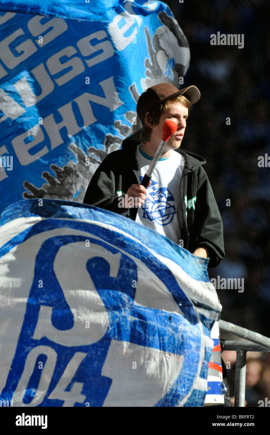 Sostenitore del club calcistico tedesco Schalke 04 batte un tamburo tra bandiere Foto Stock