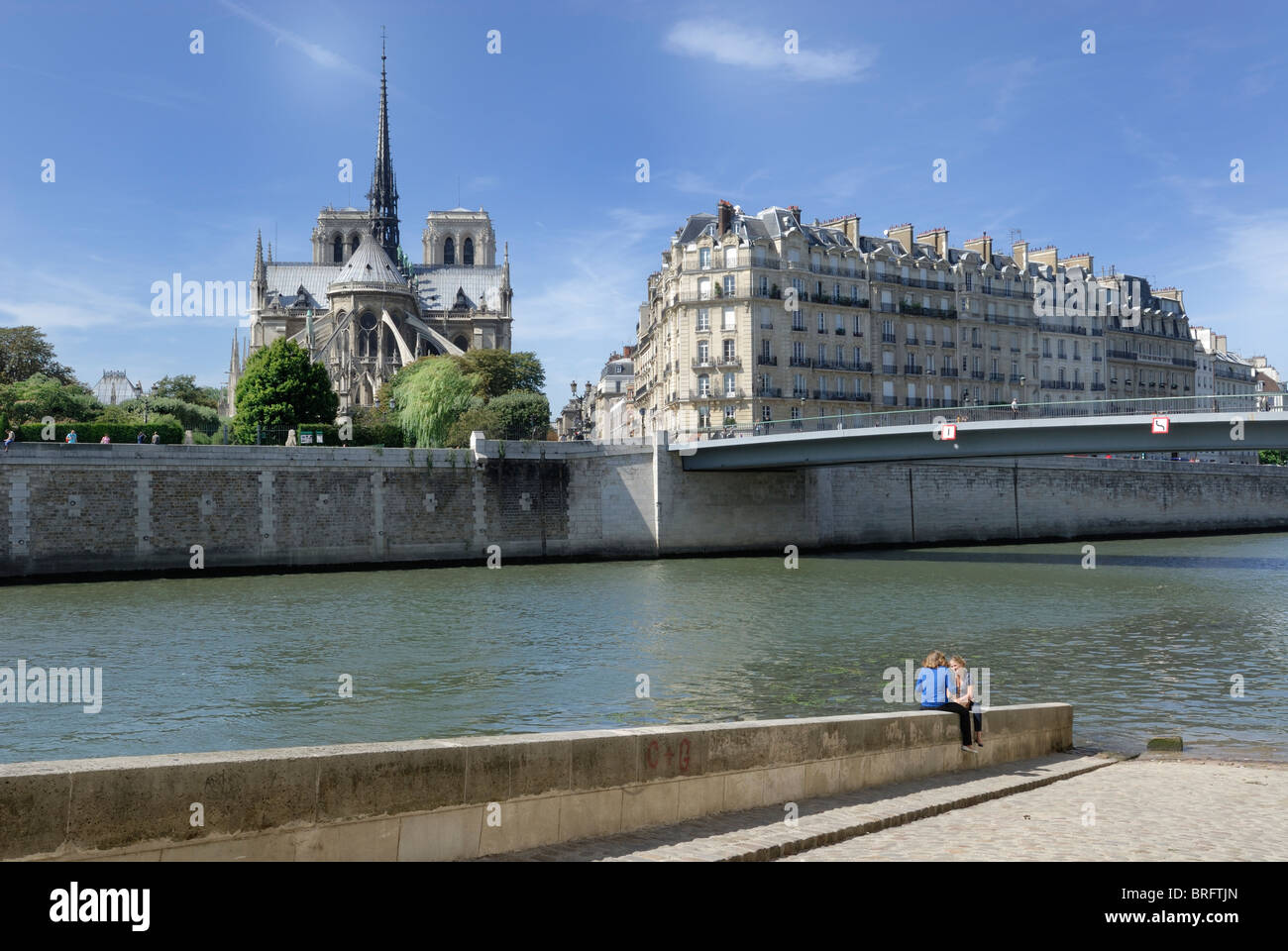 Due femmine seduto su una parete in corrispondenza del bordo del Fiume Senna con la cattedrale di Notre Dame in background, e gli edifici residenziali accanto a Foto Stock