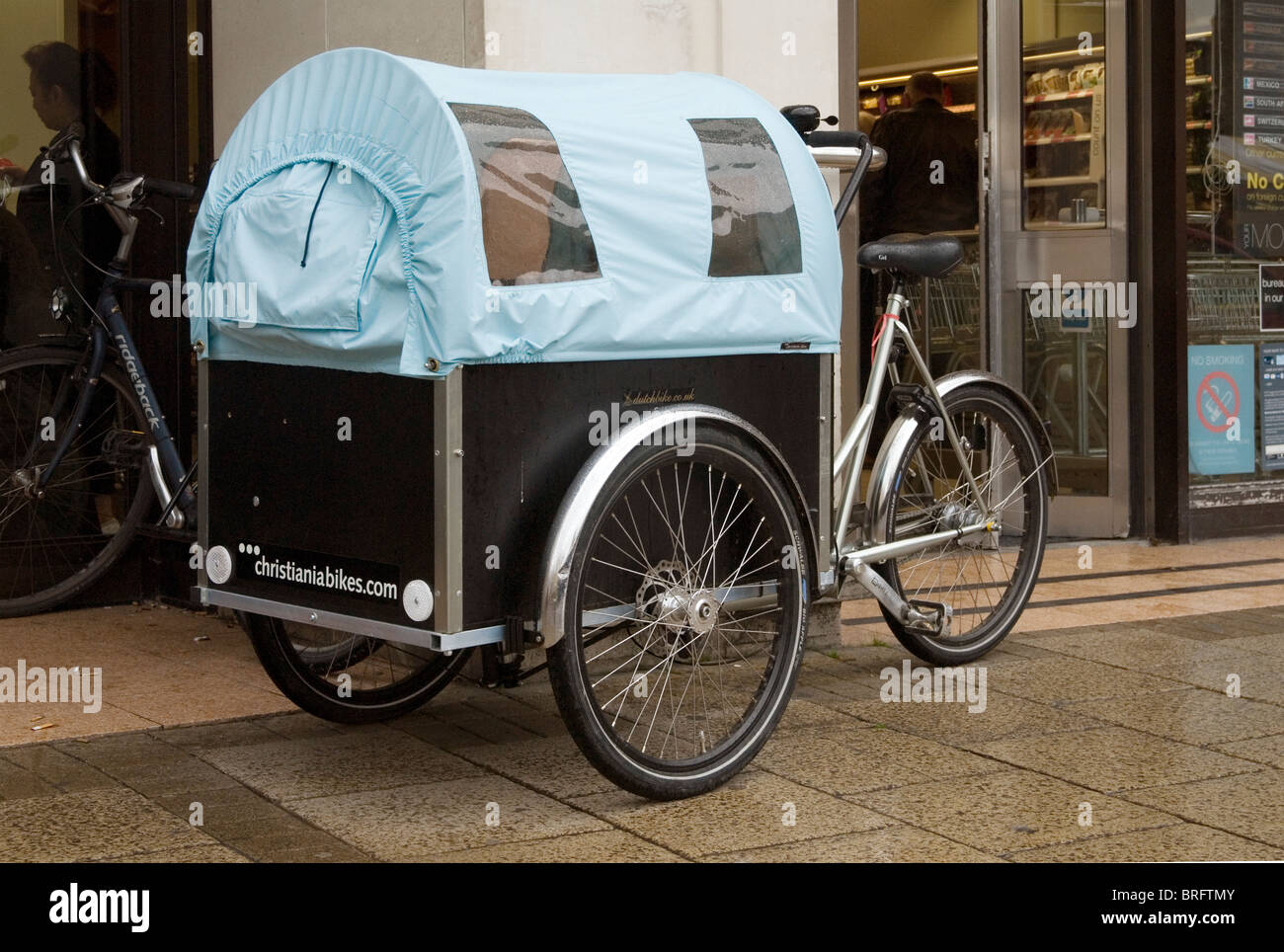 Un cargo bike presso l' impresa danese Christiania, equipaggiato per il trasporto di bambini, parcheggiato al di fuori di una città di Cambridge center store. Foto Stock