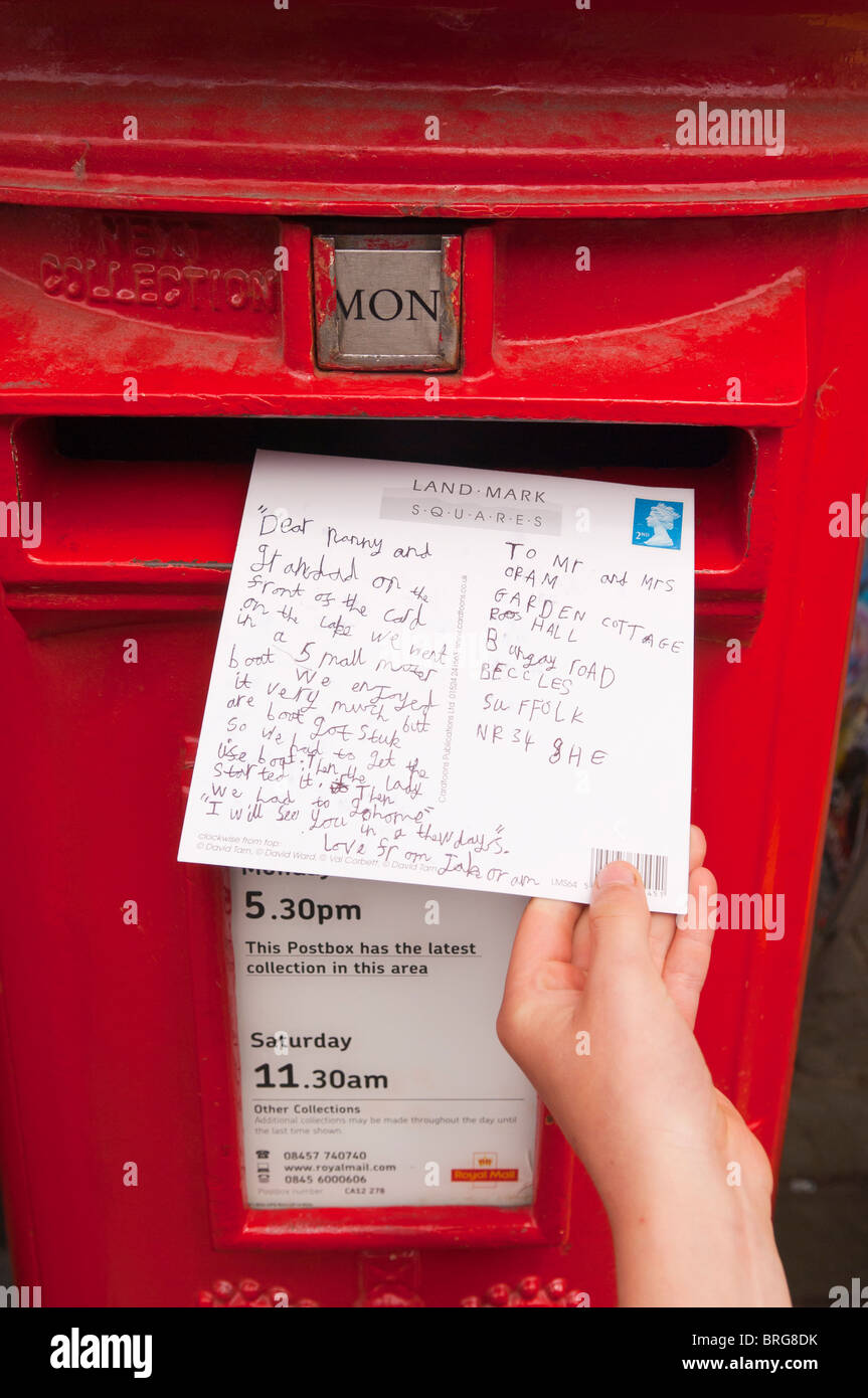 Un bambino posti una cartolina in un Royal Mail postbox nel Regno Unito Foto Stock