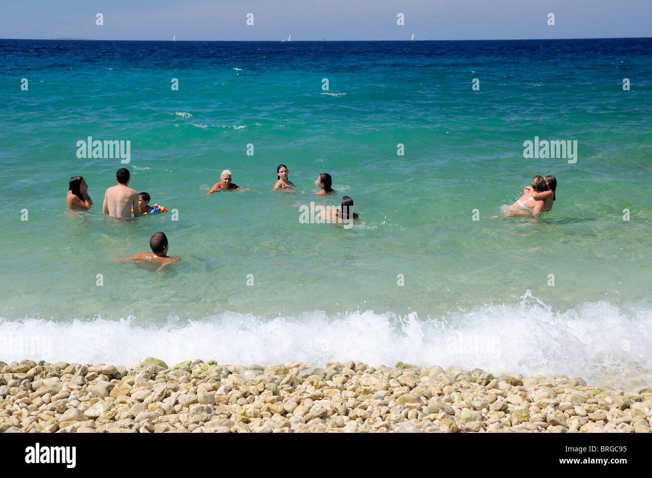 Gruppo di persone a nuotare in un mare, godendo in piccole onde luminose durante il giorno soleggiato, isola di Silba, Croazia Foto Stock