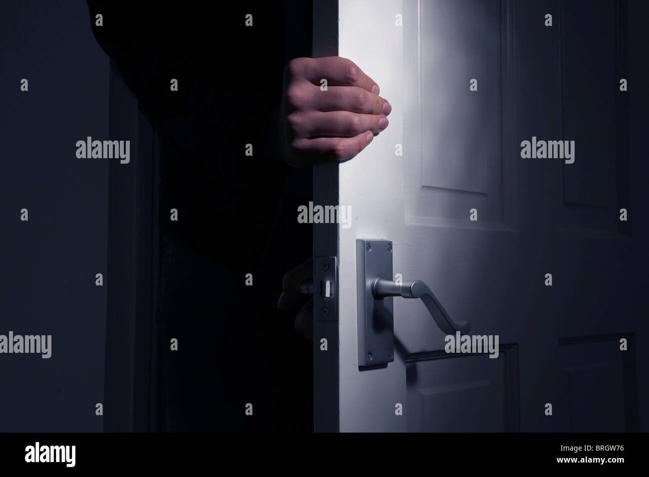 Maschio di mano in presa la porta di una stanza buia come esso viene aperto Foto Stock