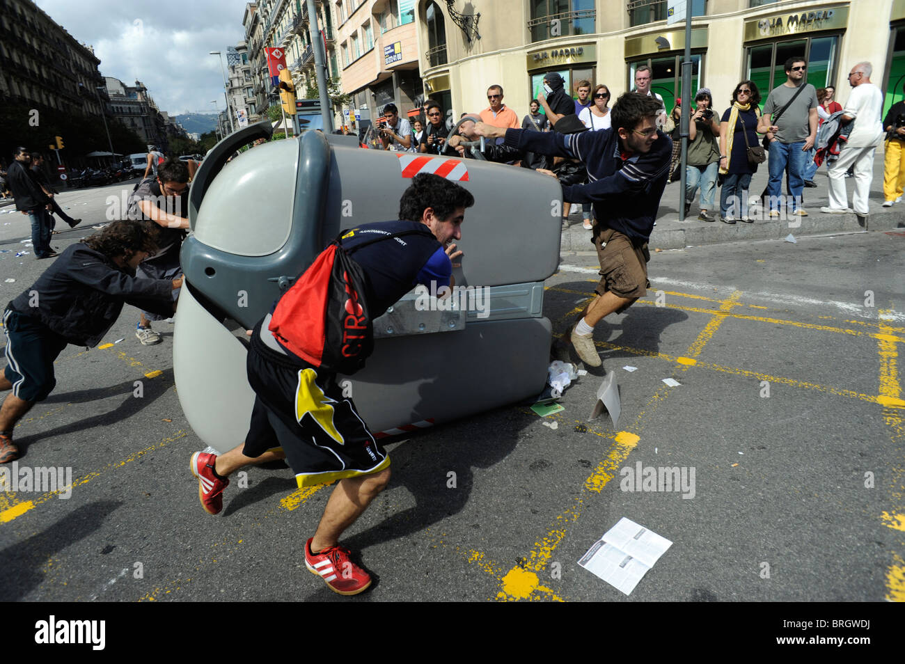 I dimostranti spingendo un contenitore durante gli scontri con la anti polizia di Barcellona durante lo sciopero generale in Spagna. Foto Stock