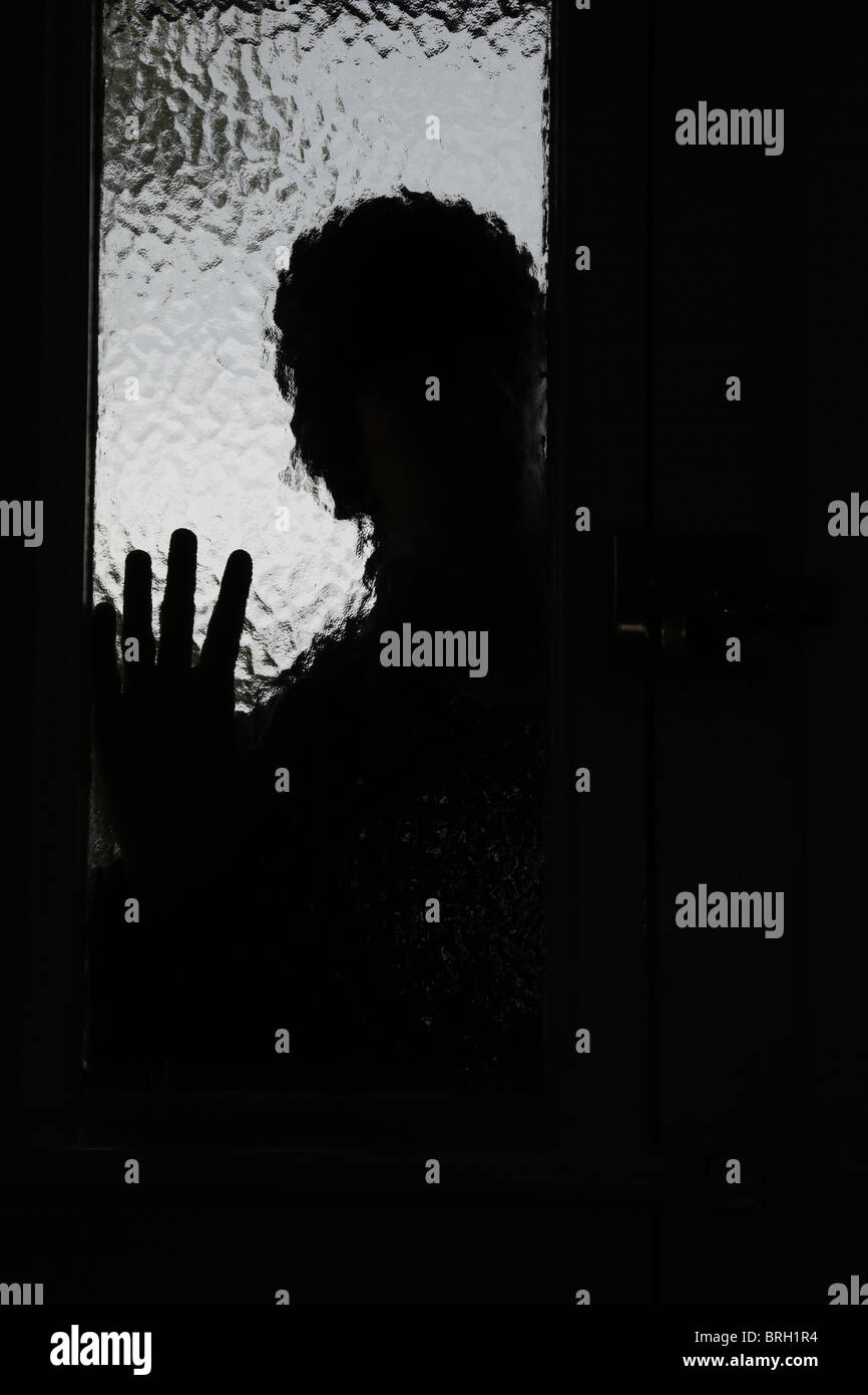 Silhouette di un intruso maschio di guardare attraverso una finestra opaca accanto a una porta anteriore Foto Stock
