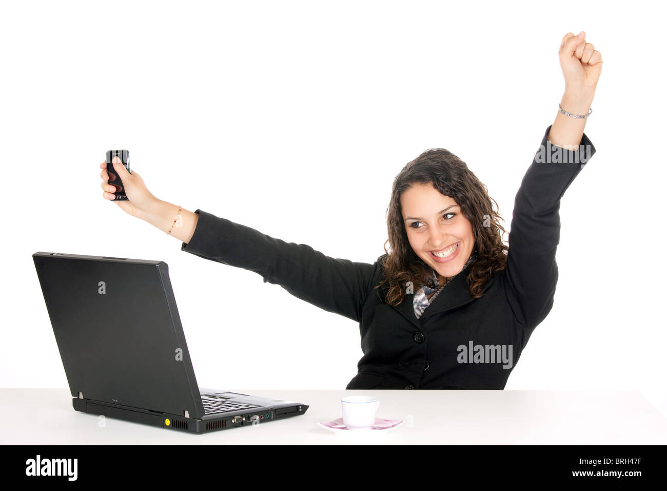 Eccitato giovane donna di affari in ufficio con computer portatile e tenendo il cellulare Foto Stock