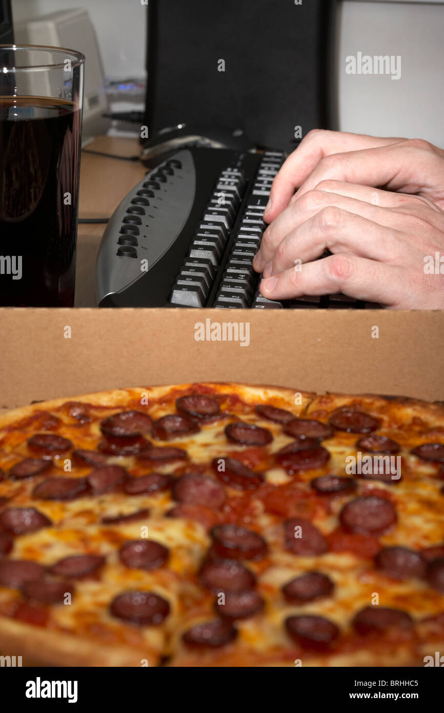 Software Engineer tirando un tutti nighter digitando su una tastiera con cola e pizza Foto Stock