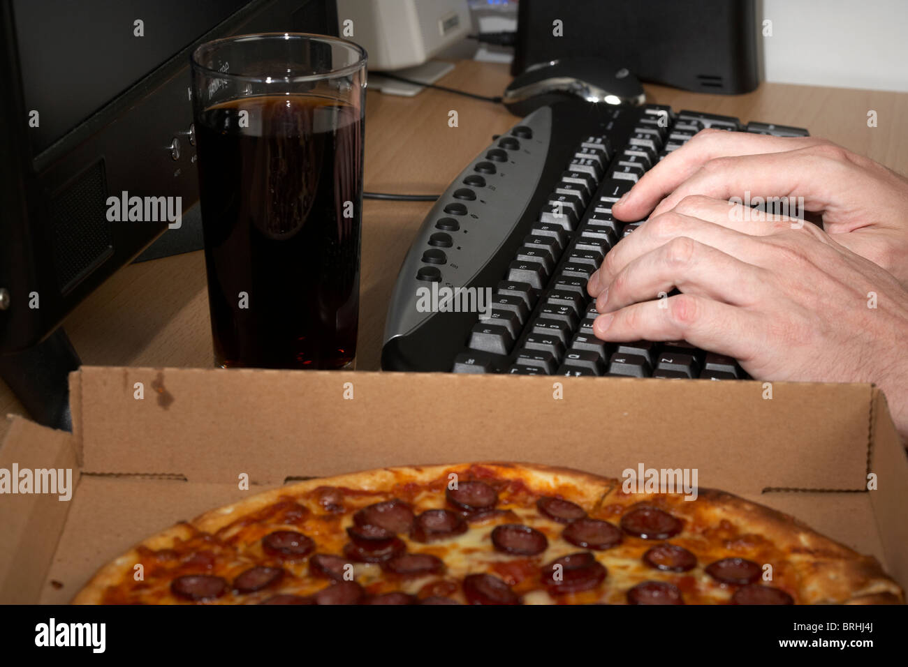 Software Engineer tirando un tutti nighter digitando su una tastiera con cola e pizza Foto Stock