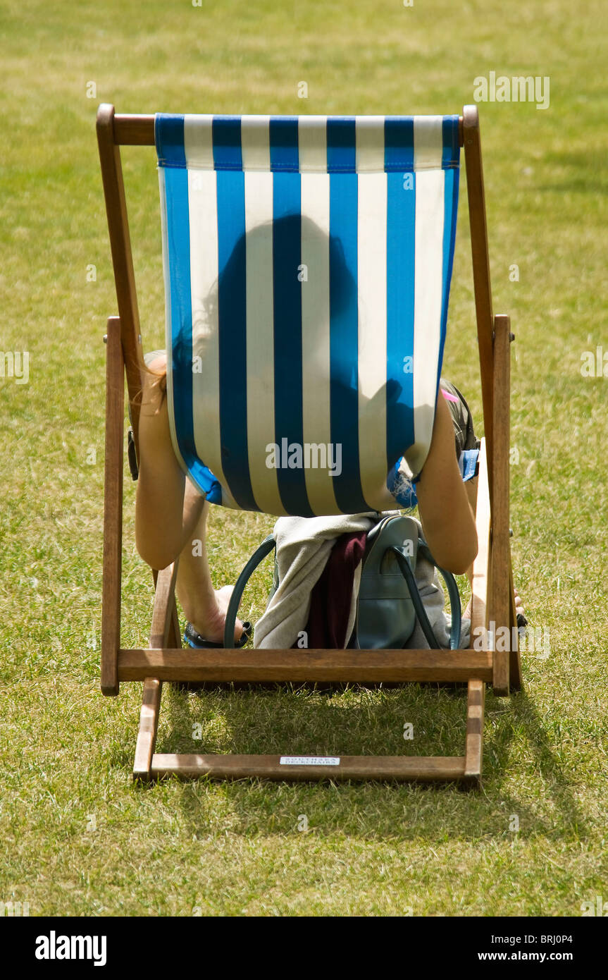 Verticale vista posteriore ritratto di una giovane donna seduta su un tradizionale Tela a strisce con sdraio per prendere il sole nel parco. Foto Stock