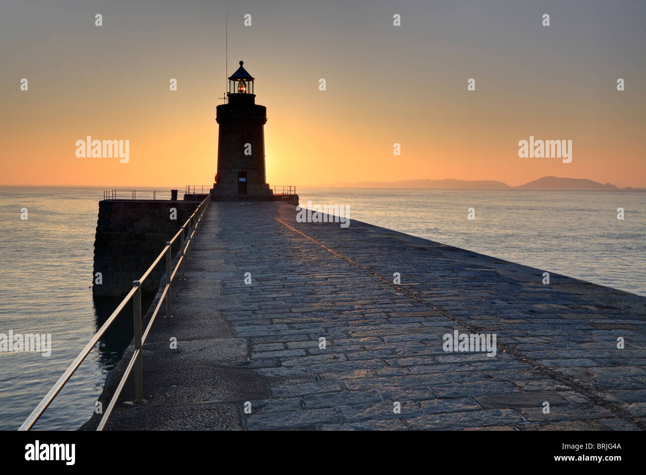 Sunrise spia si illumina di St Peter Port faro in Guernsey con l'isola di Herm profilarsi all'orizzonte Foto Stock