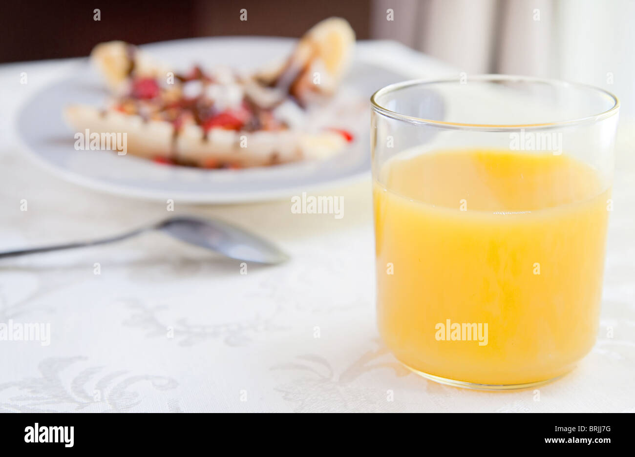 Vetro di succo d'arancia davanti a una grande prima colazione banana split Foto Stock