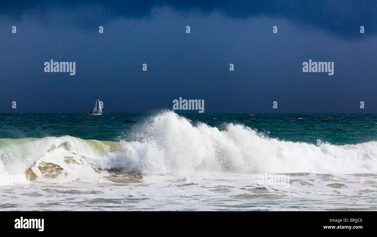 Una grande onda rottura al di sotto di un burrascoso con uno yacht in distanza. Foto Stock