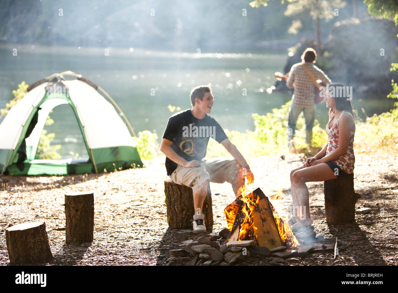 I giovani adulti camping sedersi attorno a un fuoco accanto a un lago in Idaho. Foto Stock