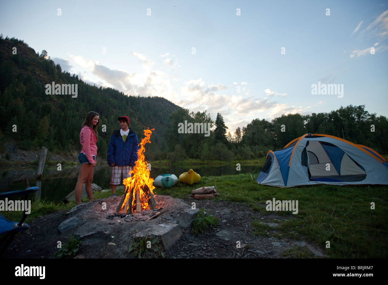 Giovane adulto giovane camping con un fuoco di campo e kayak su una bella serata estiva. Foto Stock