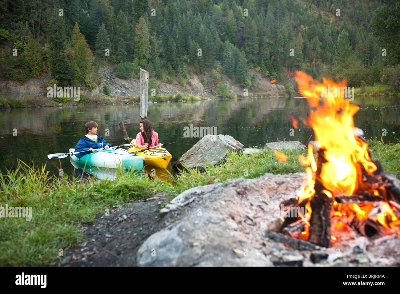 Giovane adulto giovane camping con un fuoco di campo e kayak su una bella serata estiva. Foto Stock