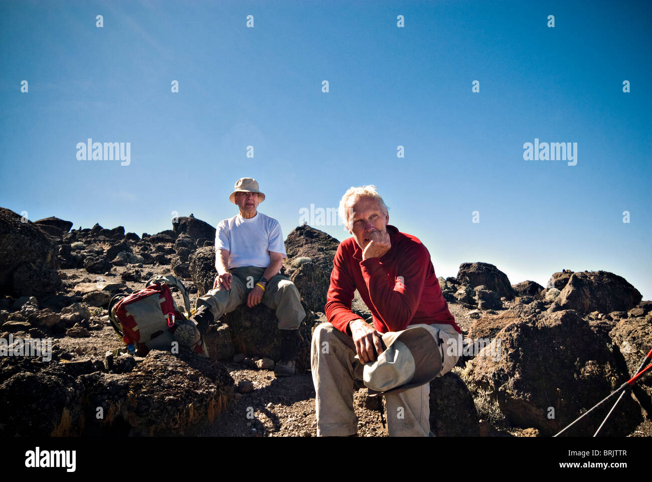 Due alti uomini hanno un resto su alcuni piccoli massi vulcanici dopo una lunga camminata fino alla vetta del monte. Di Kilimanjaro. Foto Stock