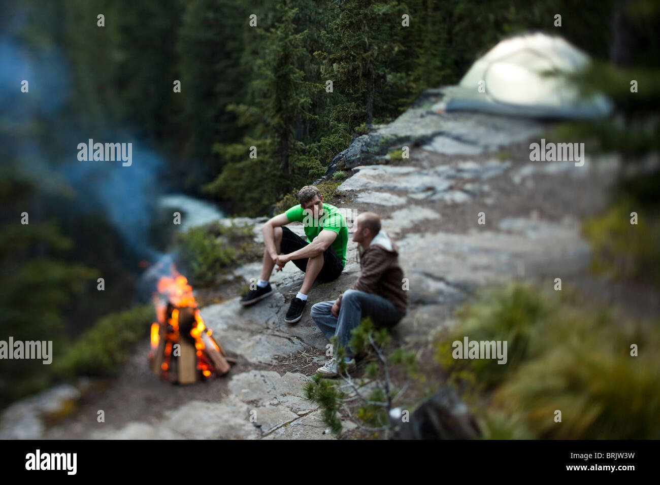 Due giovani uomini siedono attorno a un fuoco su un viaggio di campeggio in Idaho. Foto Stock