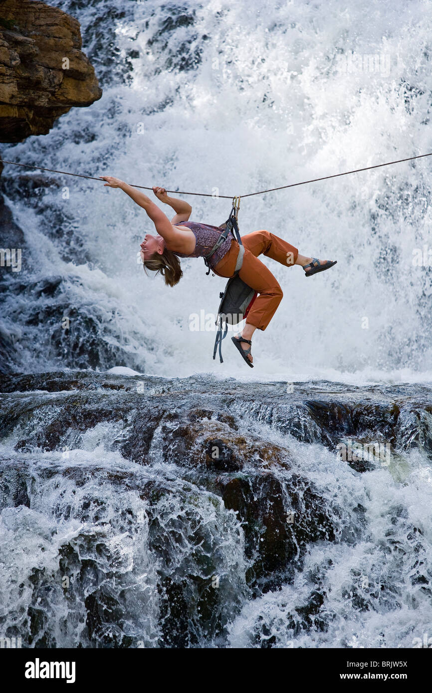 Una donna attraversa una cascata utilizzando una traversa tirolese su una fune. Foto Stock