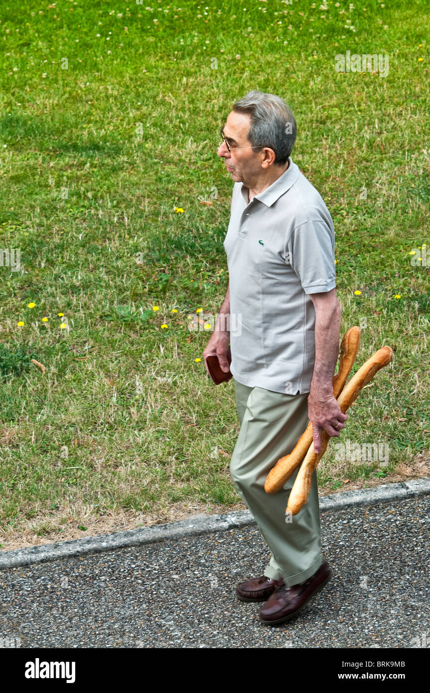 Uomo che cammina lungo il marciapiede con due baguette - Francia. Foto Stock