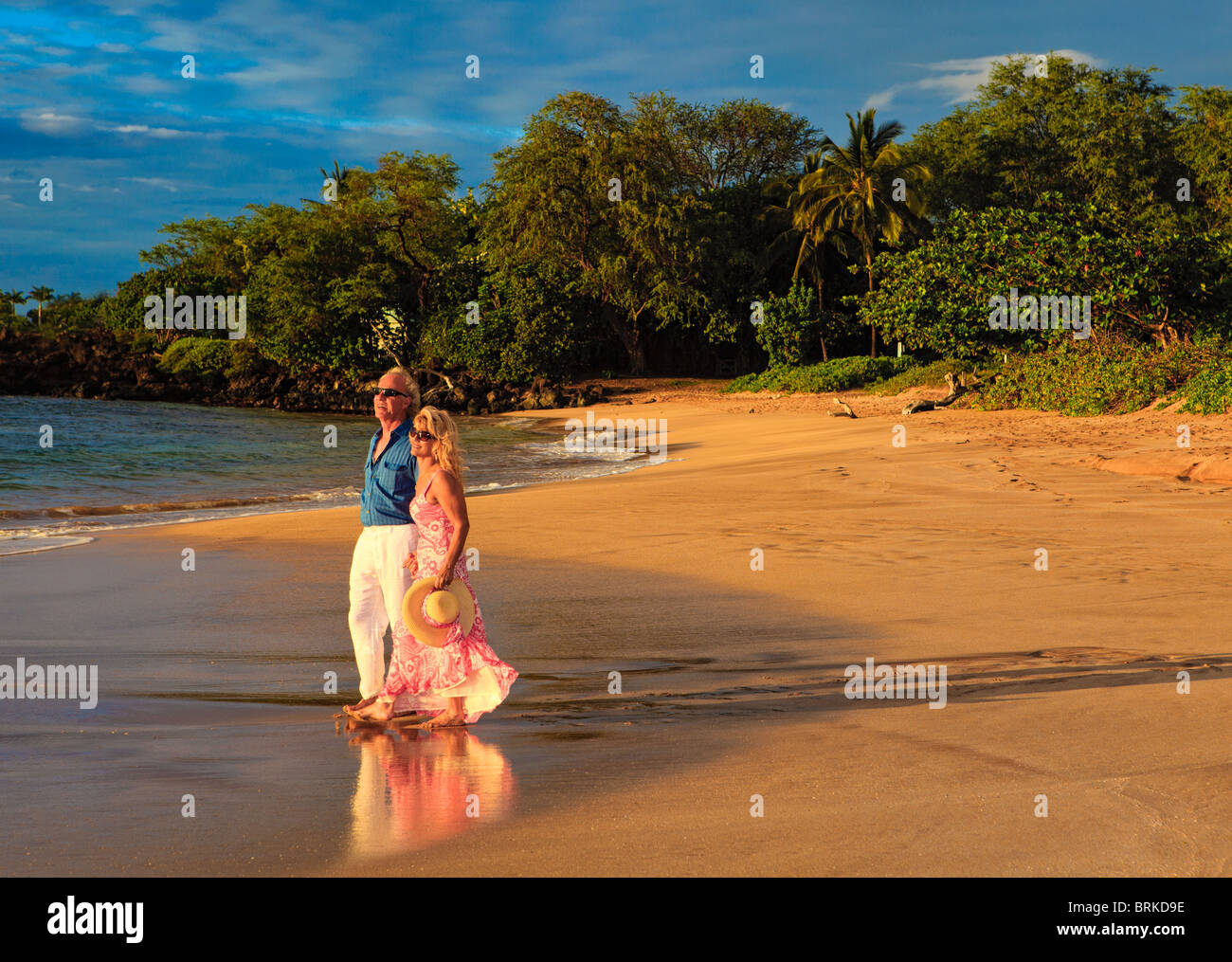 Coppia senior a camminare su una spiaggia di Maui al tramonto Foto Stock